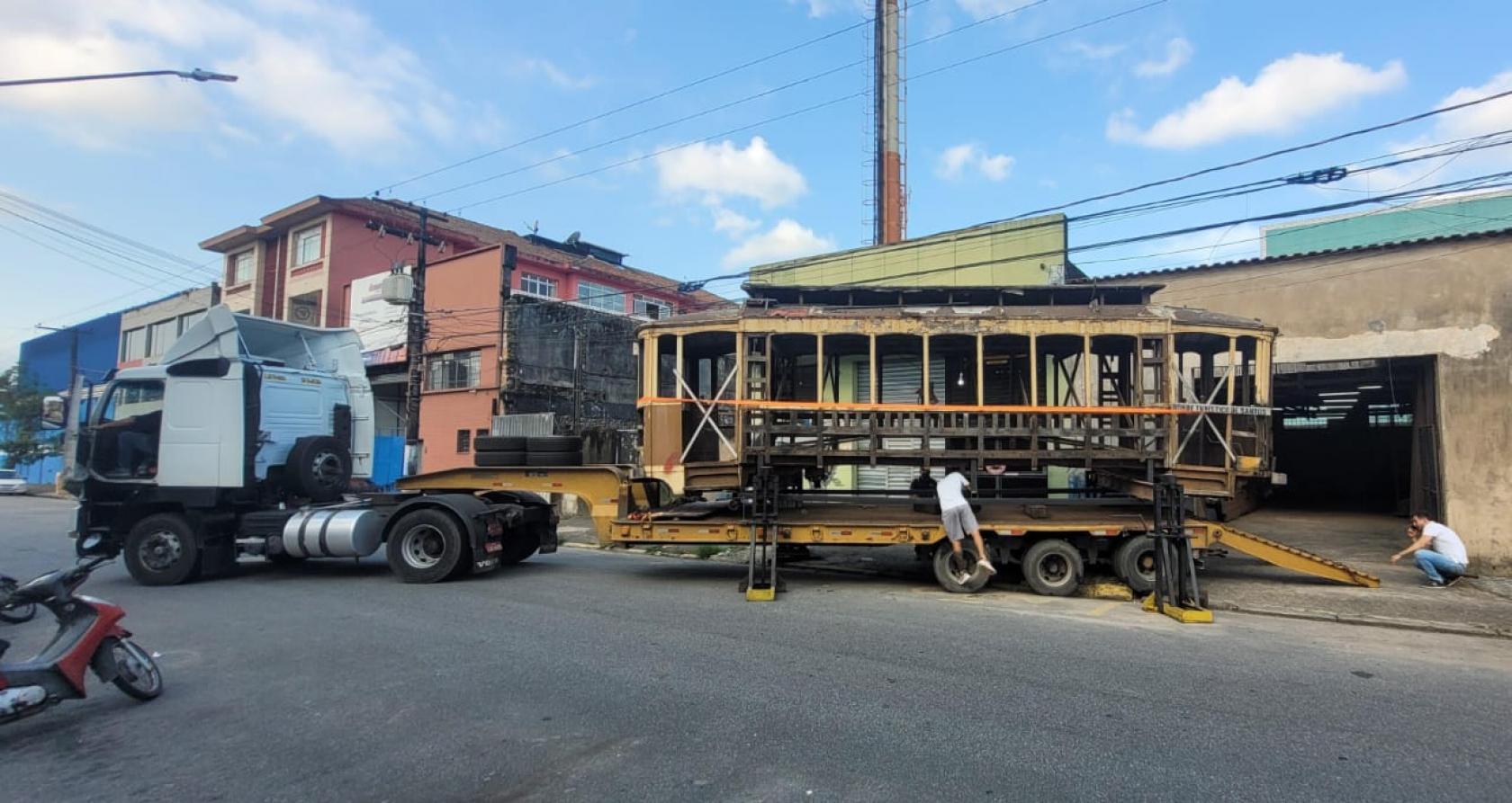 Antigo bonde é transportado de galpão por carreta. #paratodosverem
