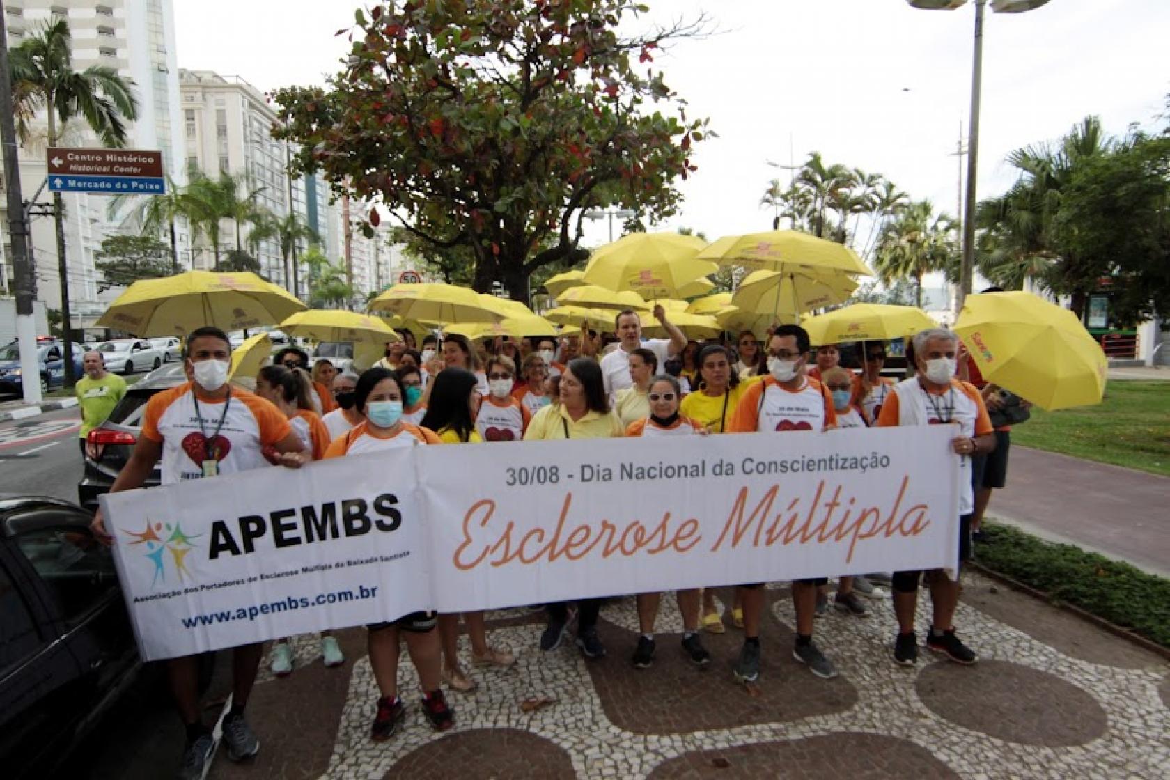 pessoas na caminhada com faixa e guarda chuvas amarelos #paratodosverem