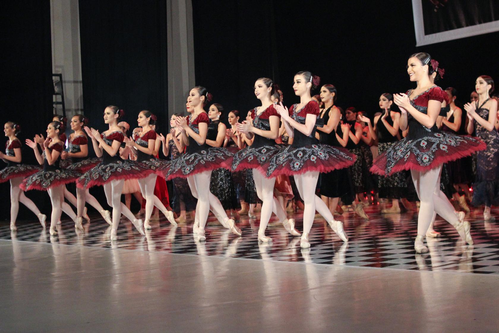 Bailarinas estão em pé enfileiradas no palco. Elas batem palmas. #Pracegover