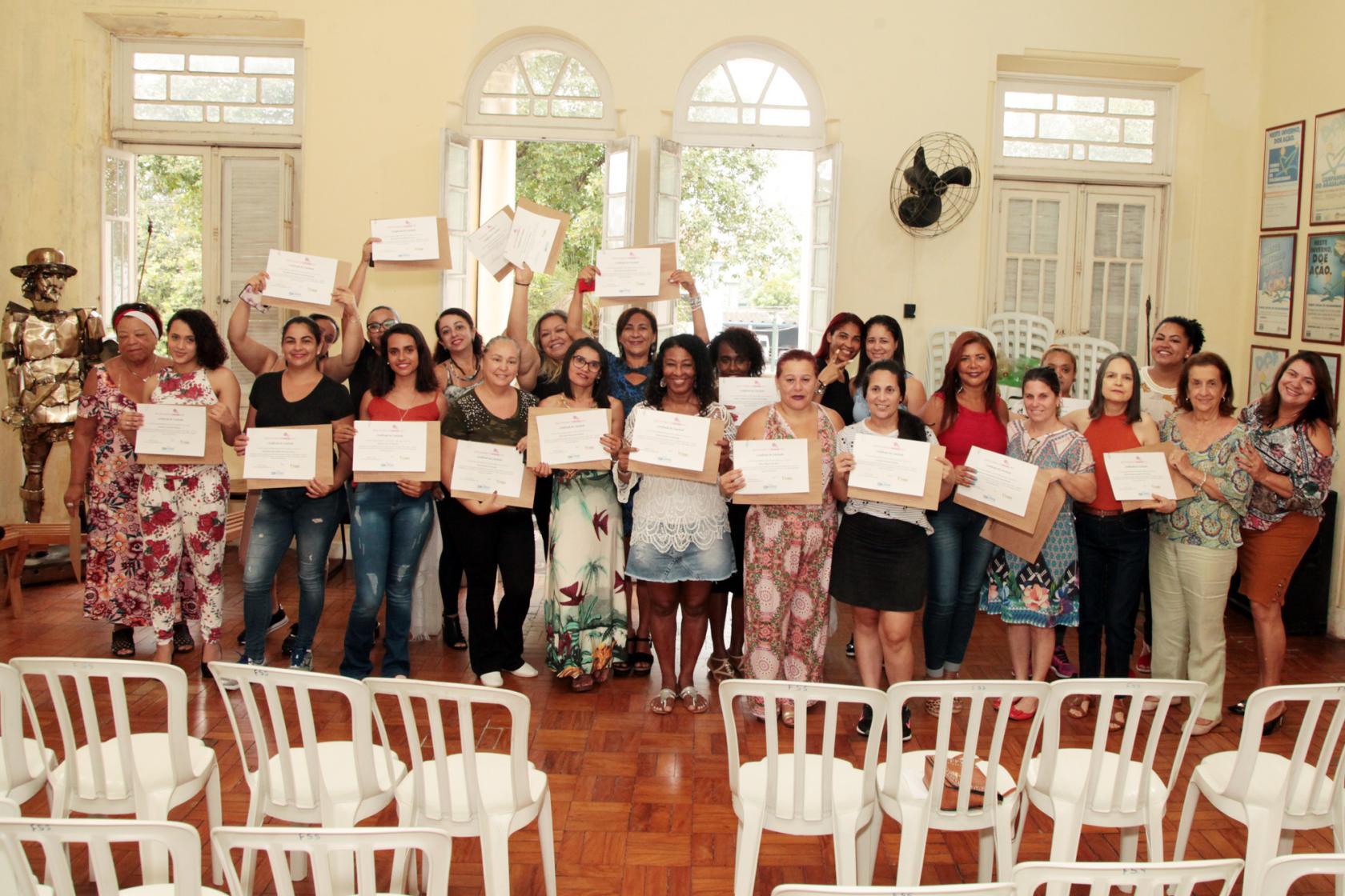 Formandas estão em pé, todas juntas, exibindo seus certificados de curso. #Pracegover