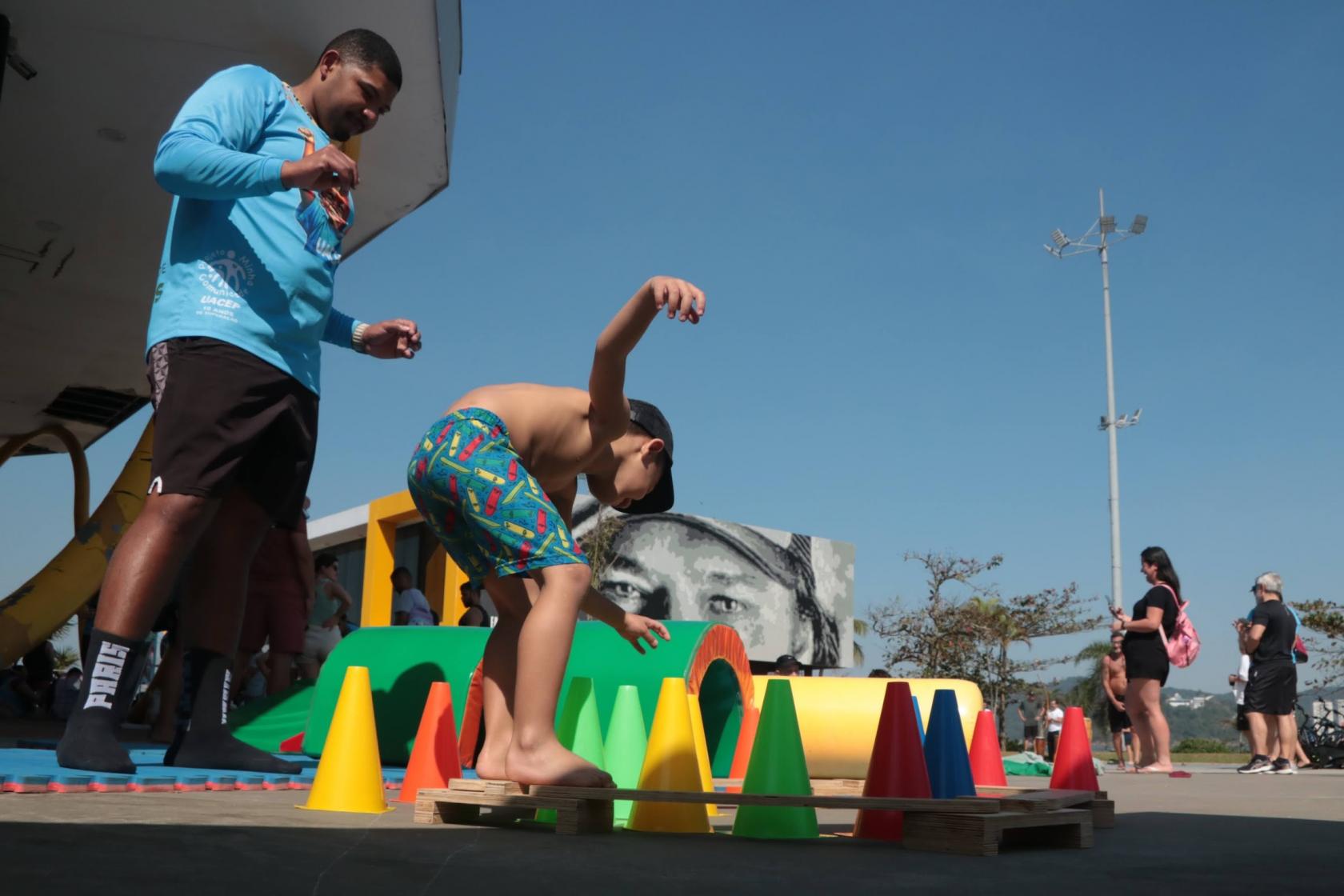 menino brinca de se equilibrar entre cones. O pai observa.#paratodosverem