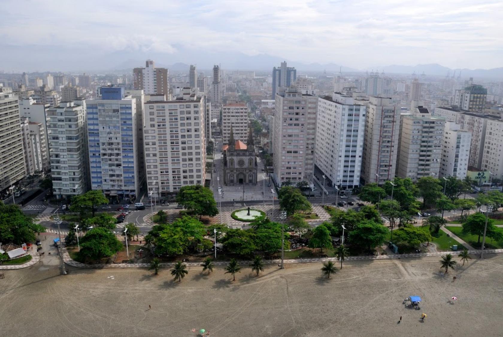 vista geral do bairro, a partir da praia, com muitos prédios ao fundo e a igreja ao centro. #paratodosverem