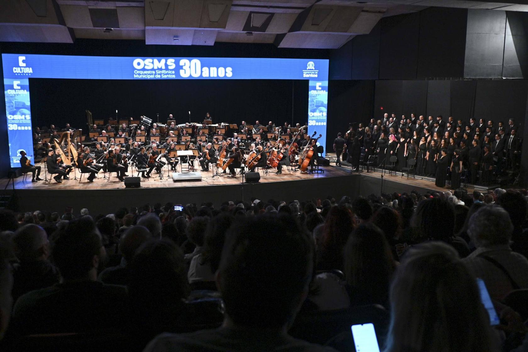 plateia e palco com músicos e coralistas. #paratodosverem