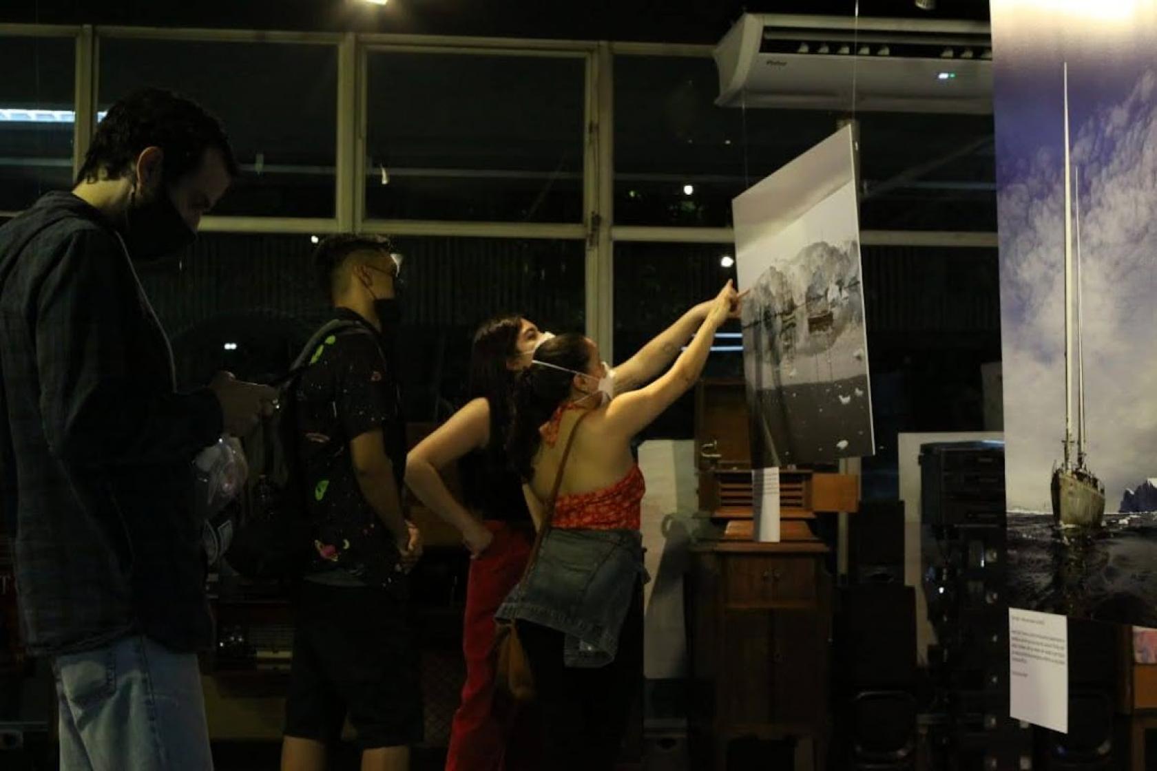 pessoas apontam para foto em exposição #paratodosverem