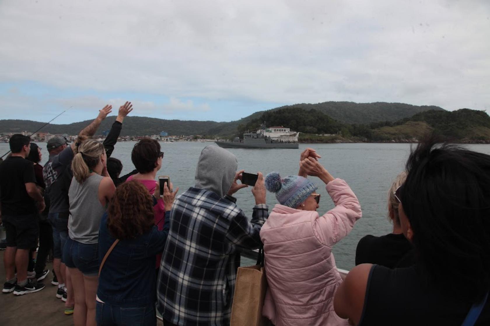 pessoas fotografam e olham navio de guerra #paratodosverem