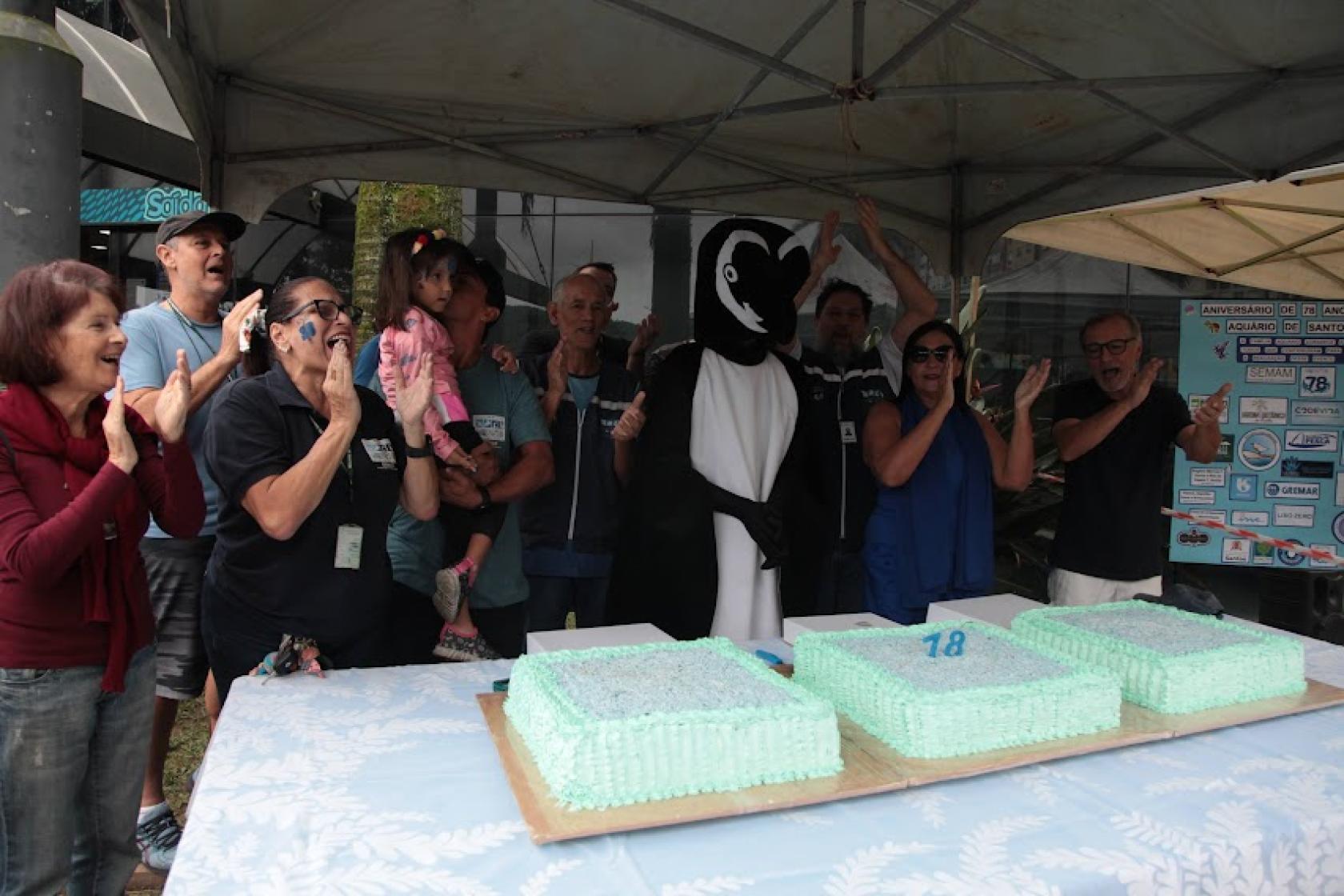 pessoas e homem fantasiado de pinguim cantam parabéns #paratodosverem