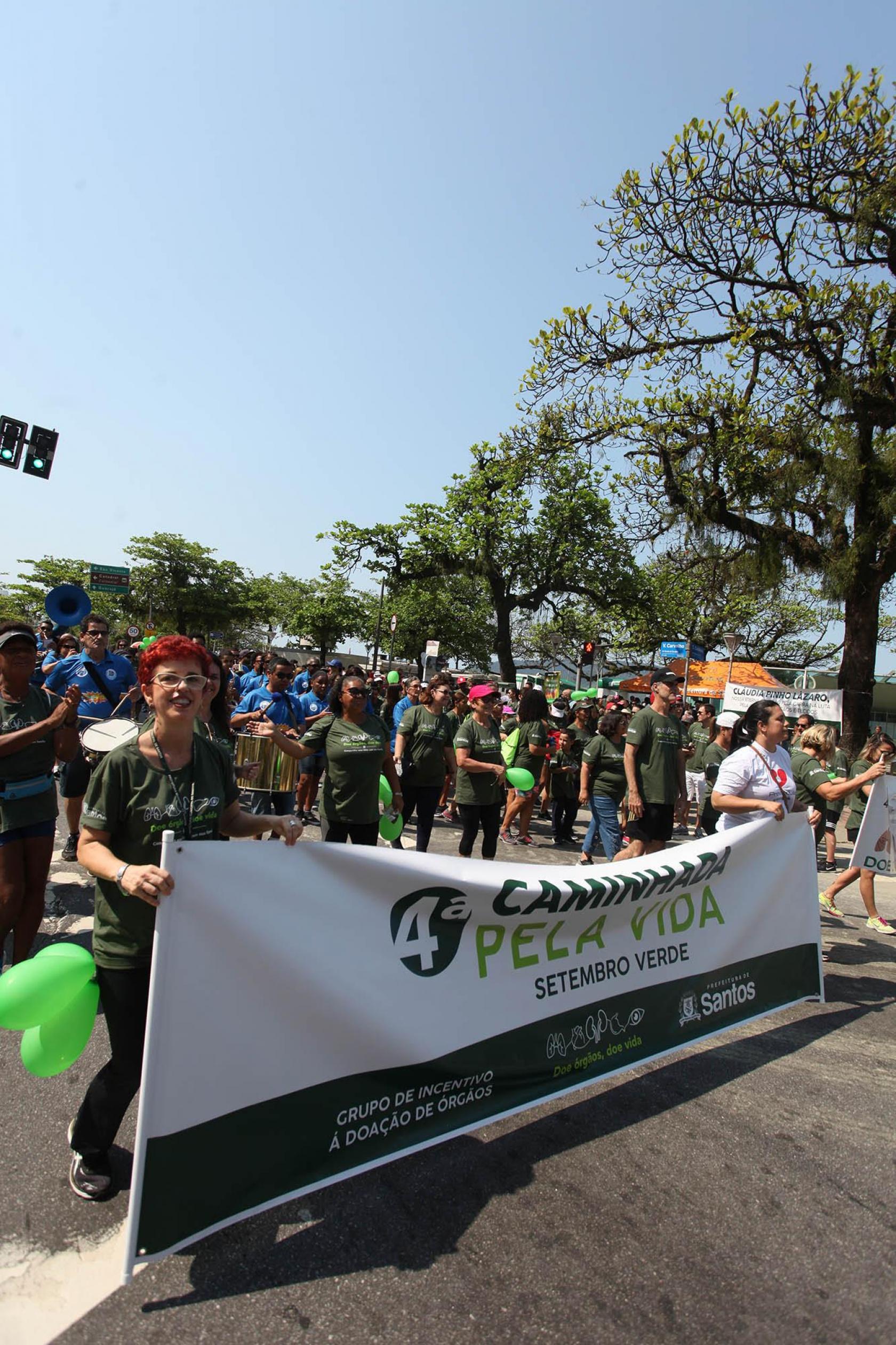 pessoas caminham com faixa da campanha #pracegover