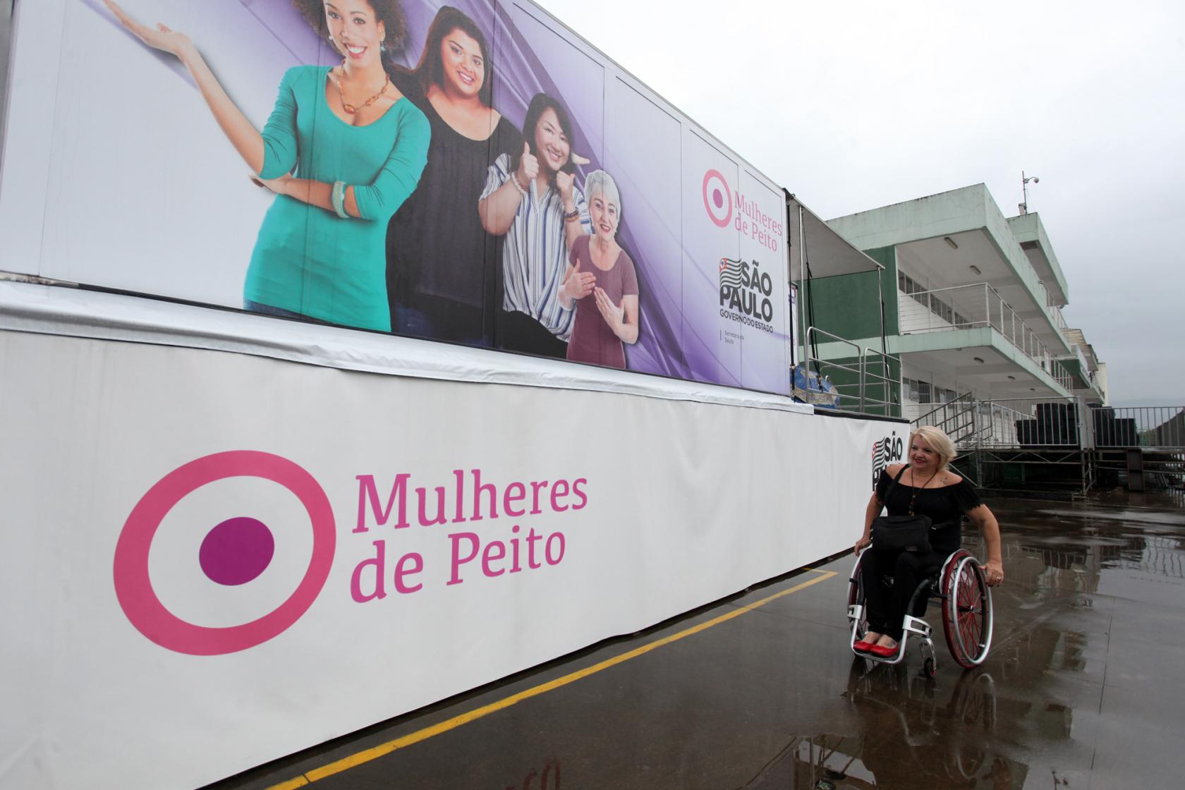 Mulher em cadeira de rodas passa ao lado de carreta #pracegover