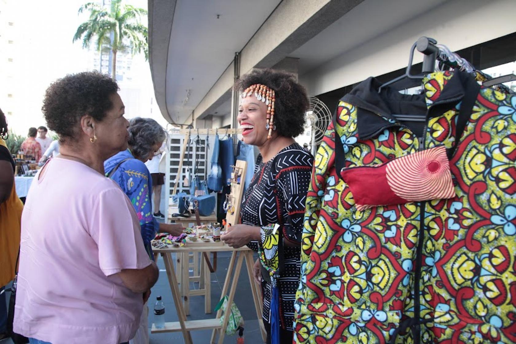 mulher fala com dona de barraca de artesanato #paratodosverem