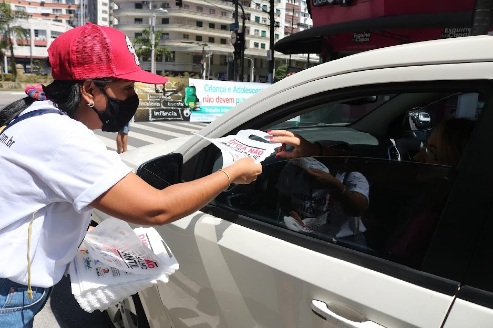 mulher distribui panfleto em carro #paratodosverem