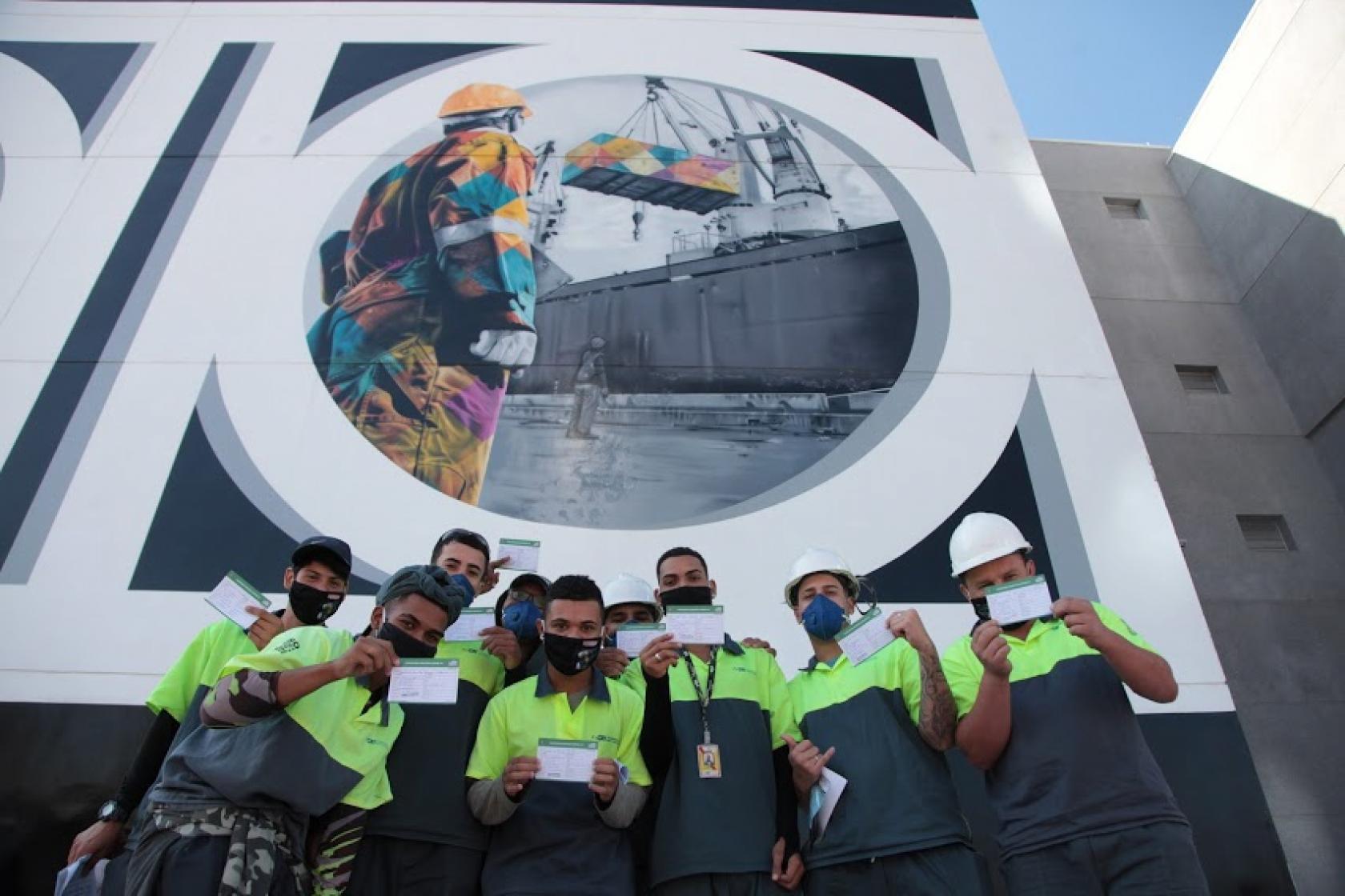 trabalhadores posam ao lado de mural que fala do porto #paratodosverem