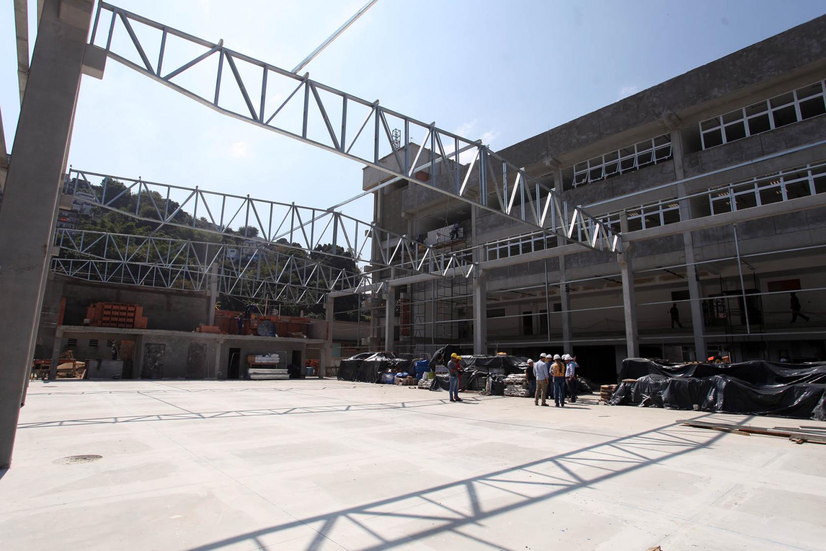 O prédio em fase de final de construção ao fundo com a estrutura metálica da cobertura da quadra à frente. #Pracegover