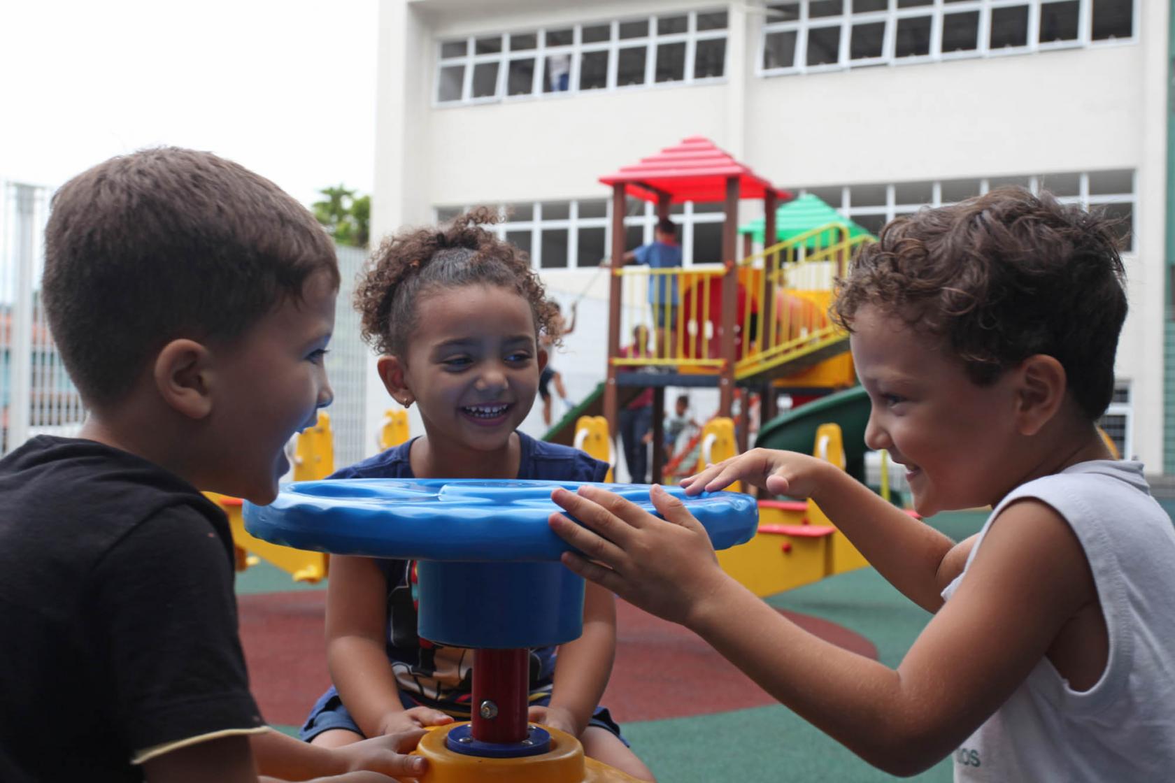 três crianças brincam no playground #pracegover 