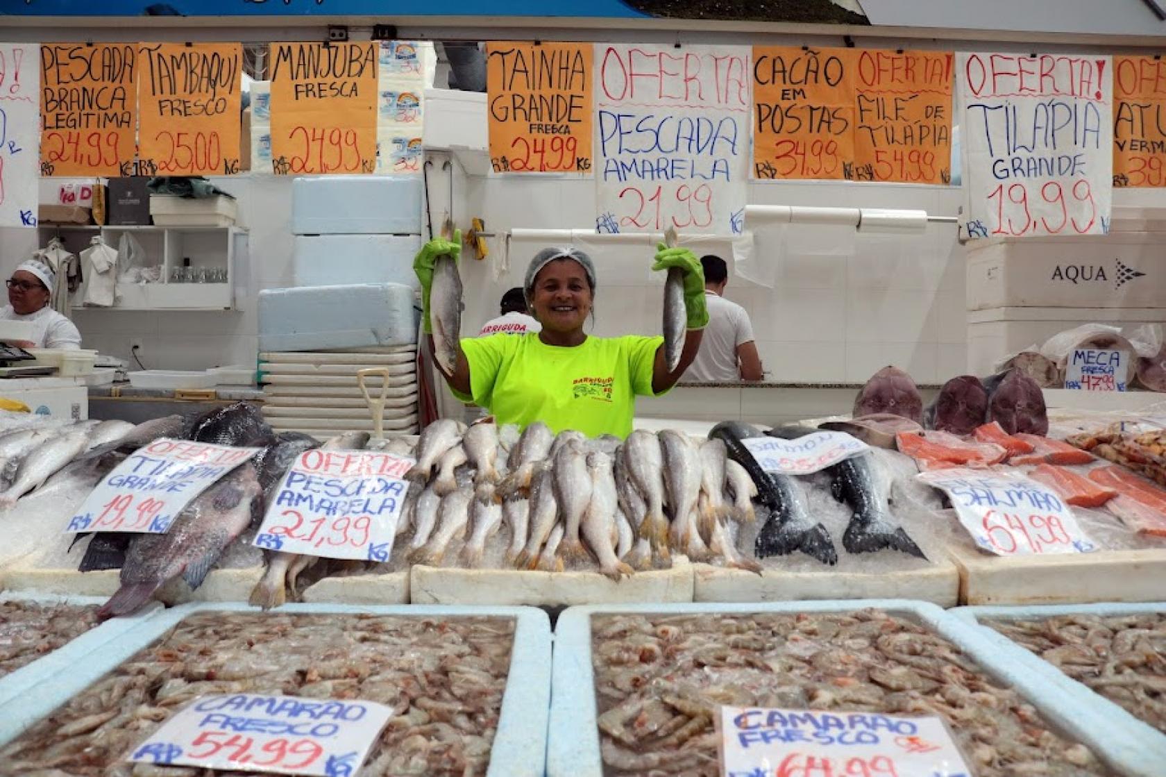vendedora mostra peixes à venda #paratodosverem