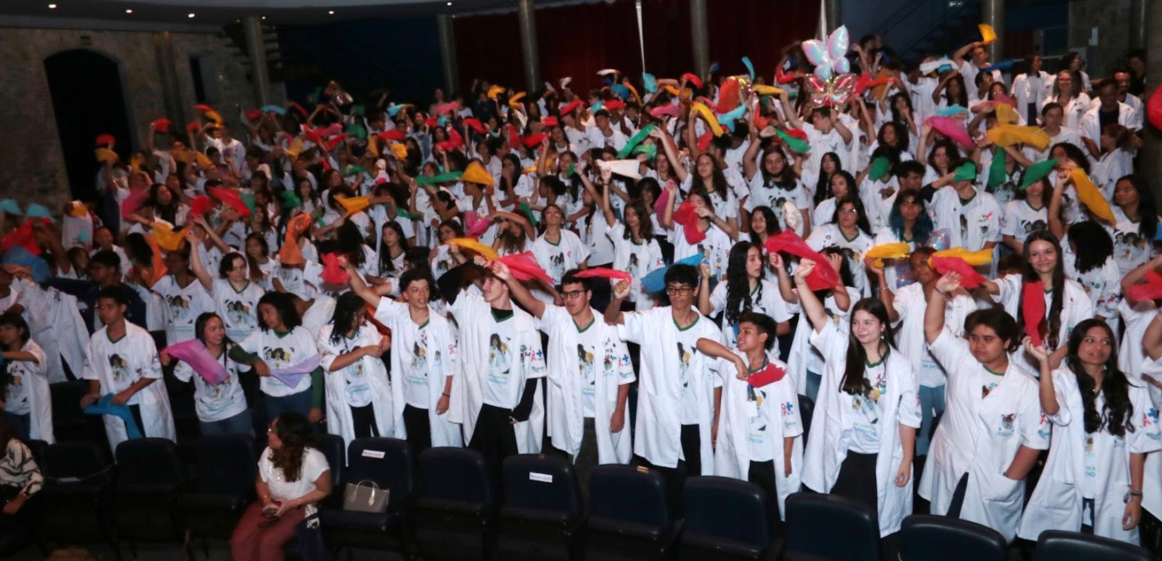 alunos formados de jaleco balançam lenços ao alto #paratodosverem