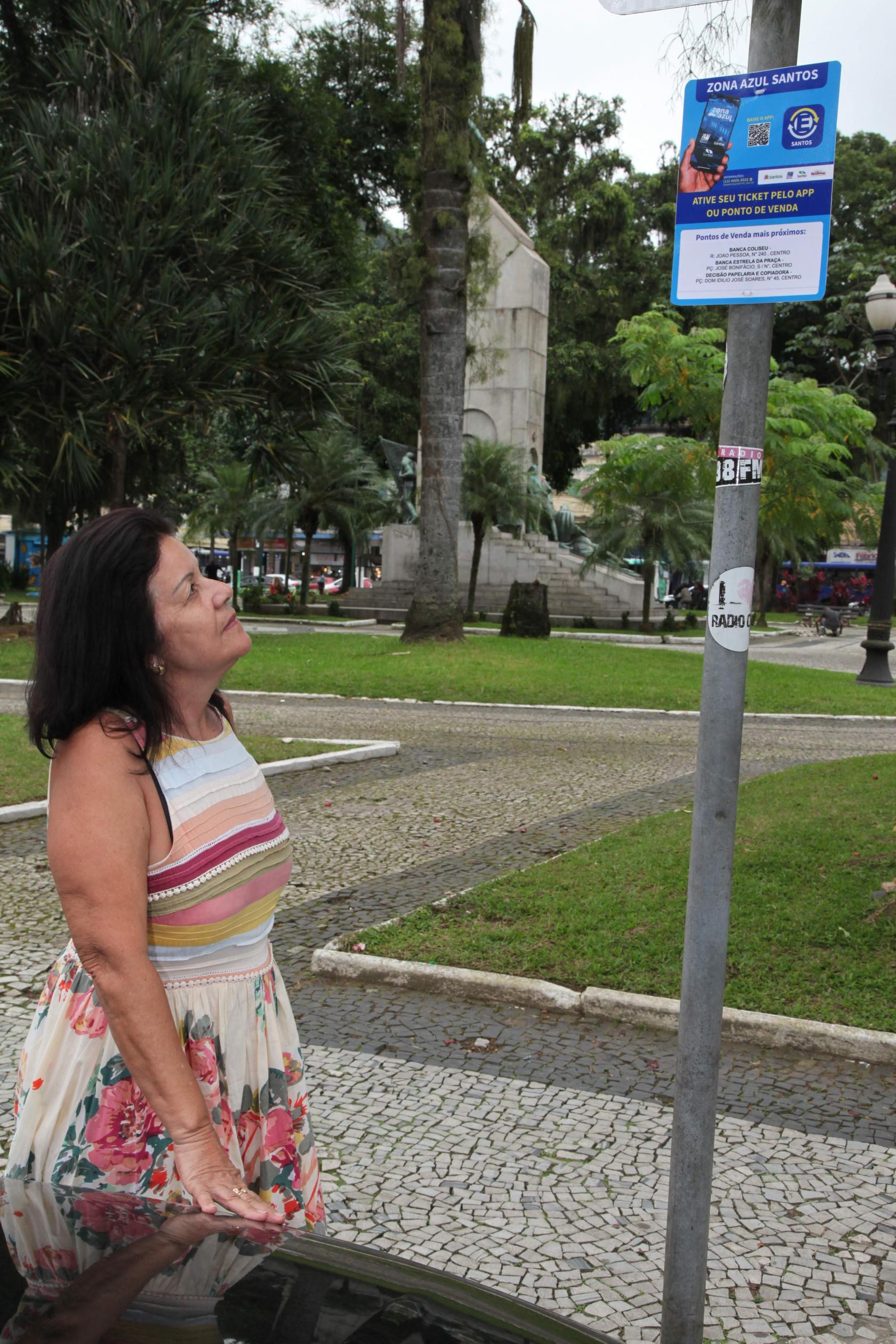 Mulher olha para placa da zona azul digital #pracegover 