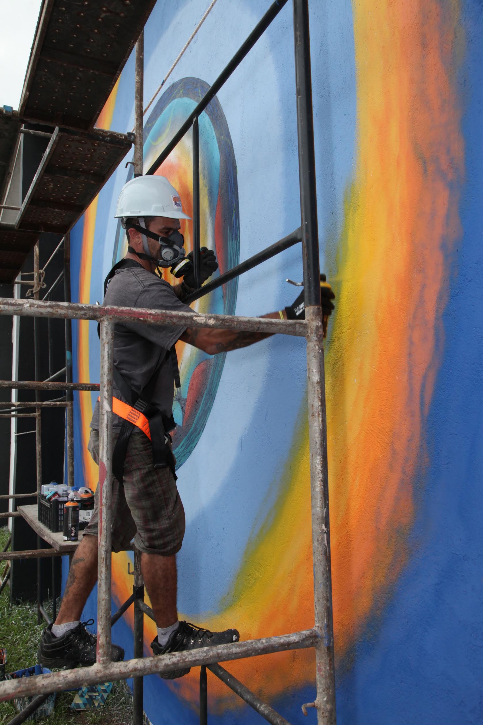homem faz grafite em muro #pracegover