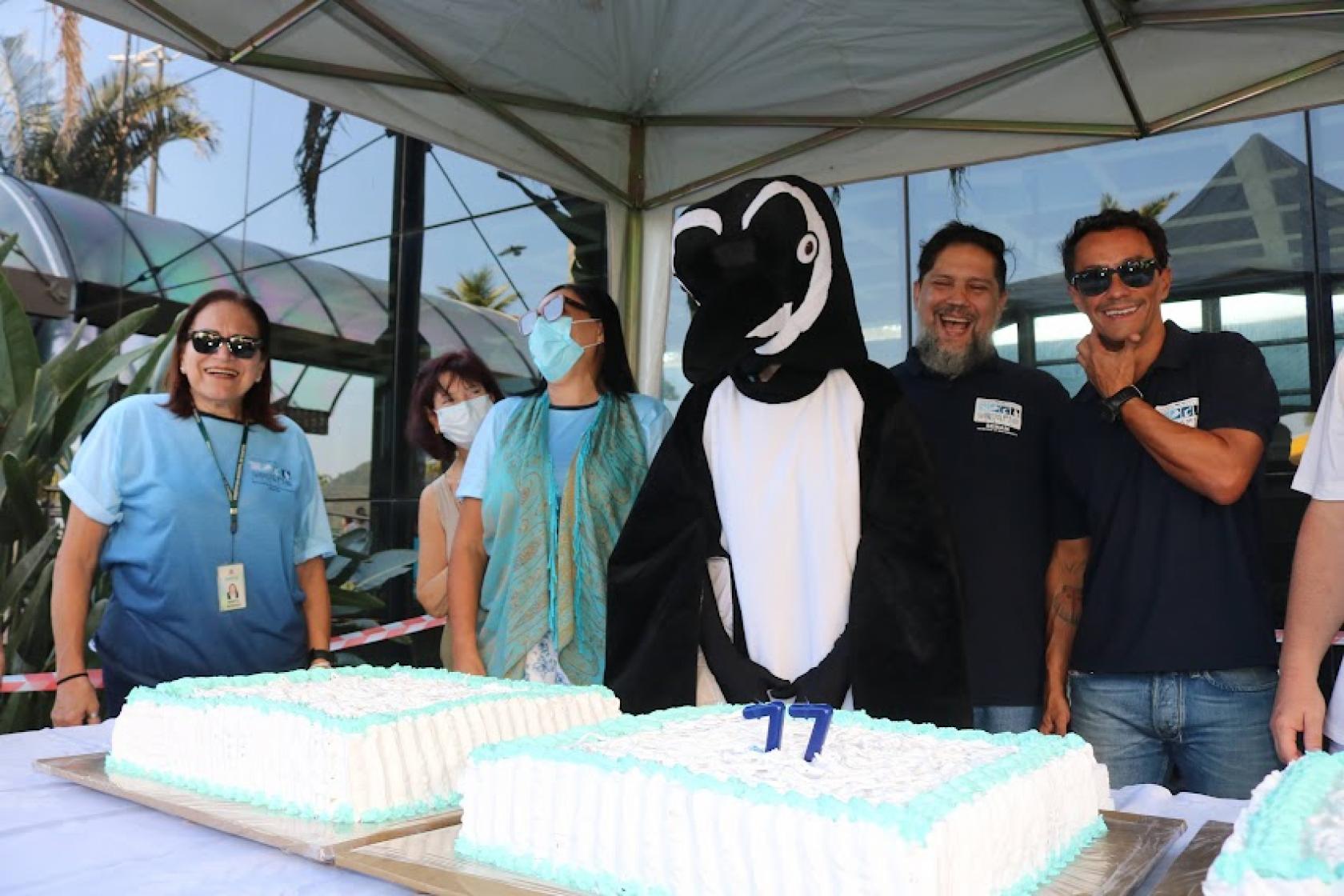 pinguim e pessoas na frente do bolo de aniversário #paratodosverem