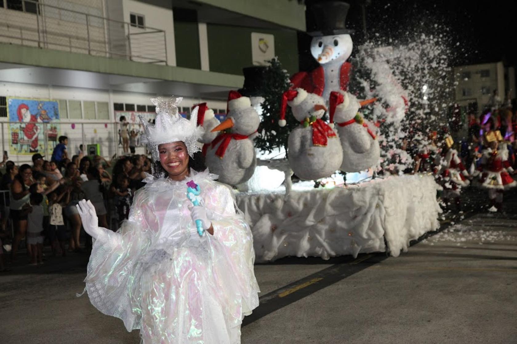 pessoa fantasiada desfila na frente de carro alegórico com boneco de neve #paratodosverem