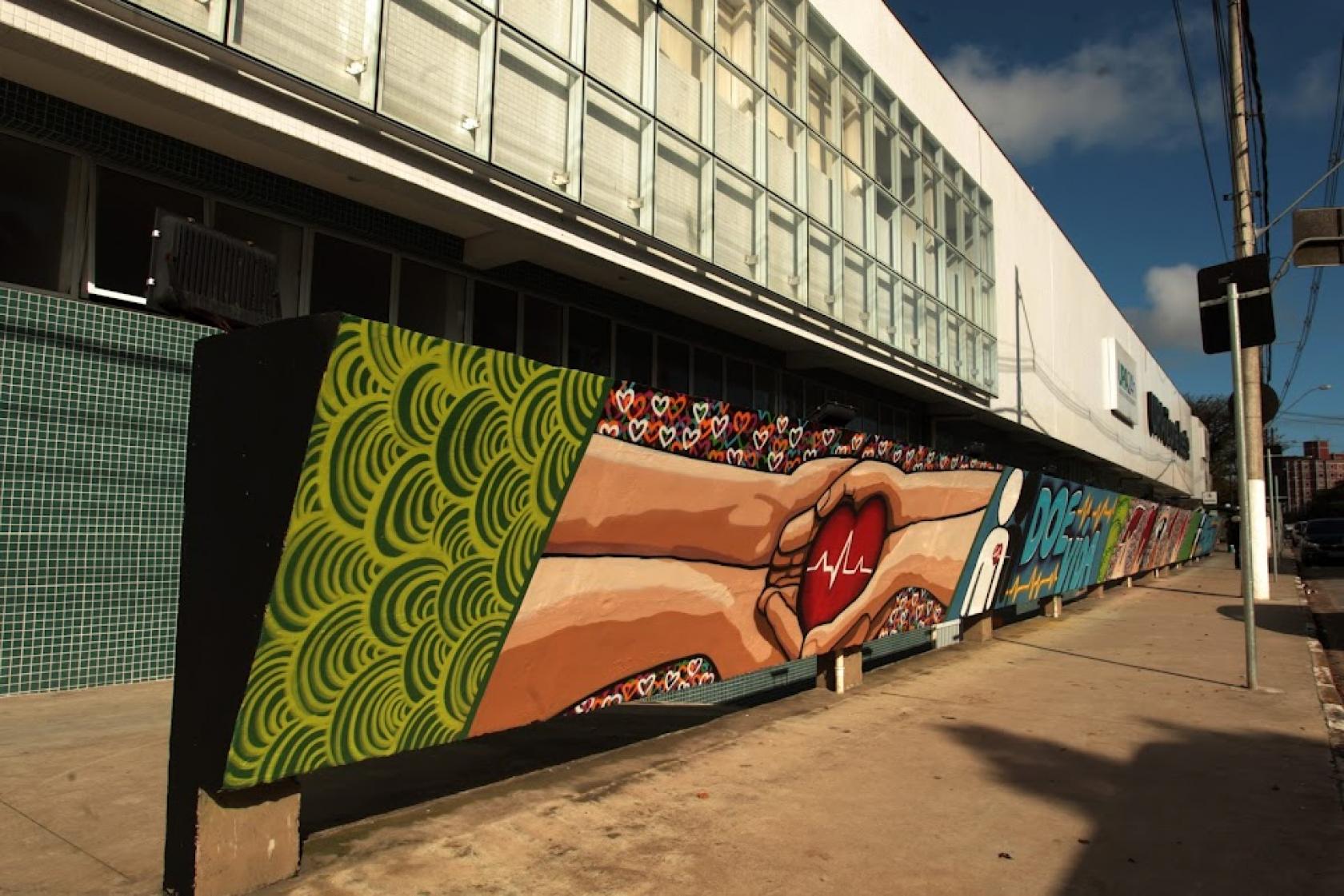 mural pintado em parede mostra quatro mãos estendidas segurando um coração. #paratodosverem
