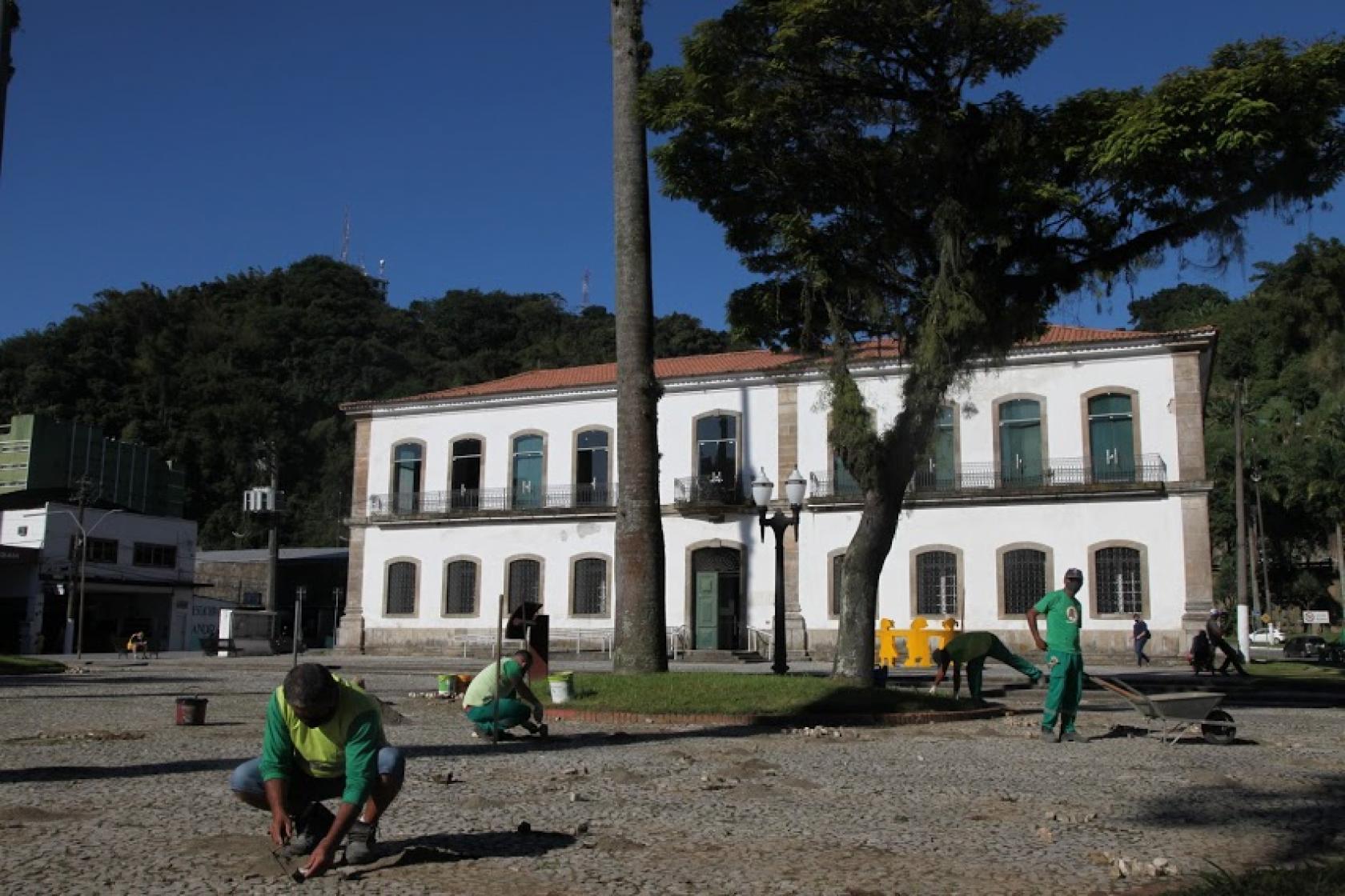 homens trabalhando no assentamento de mosaico com a Cadeia Velha ao fundo. #paratodosverem