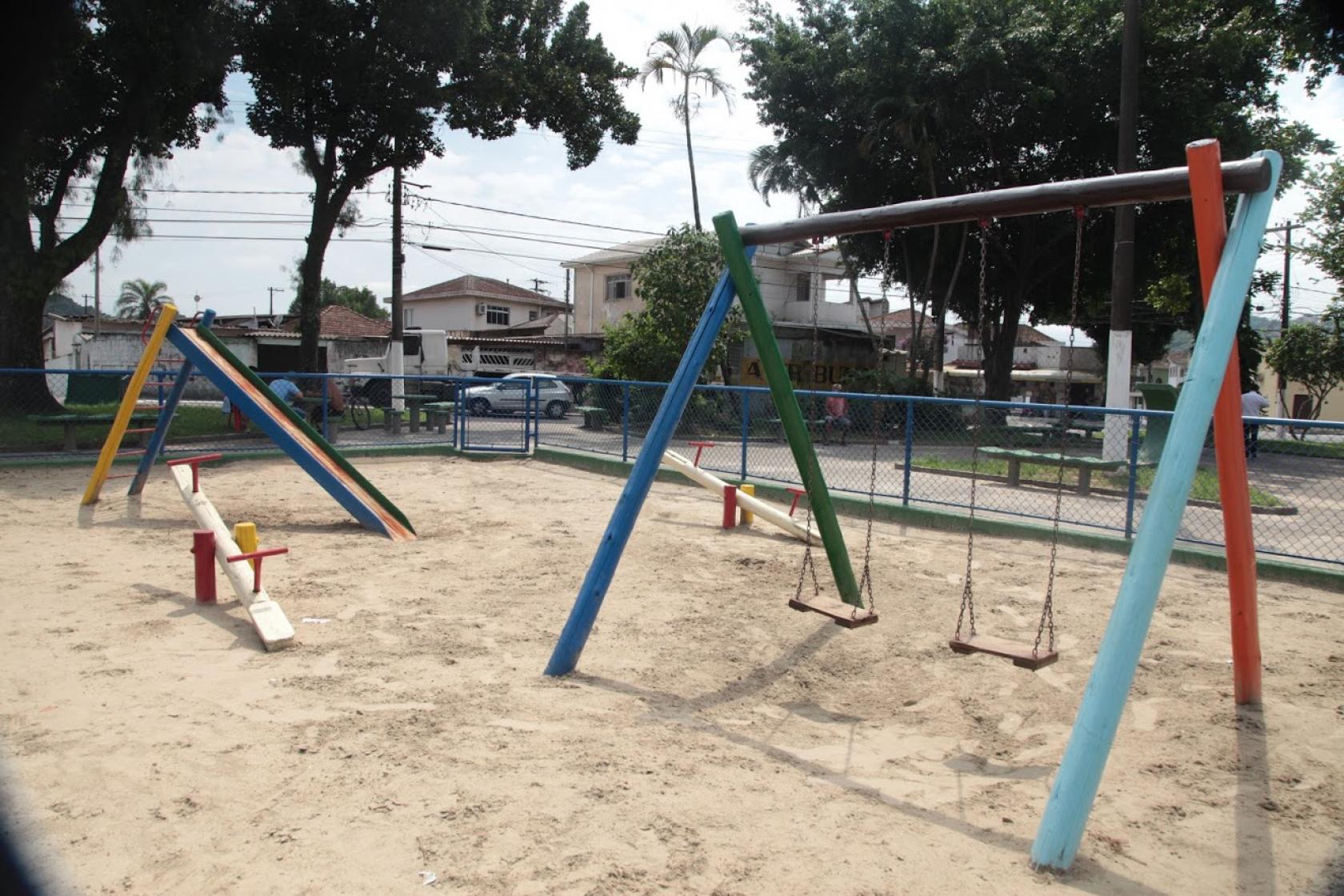 Play ground em praça, com conjunto de dois balancês, uma gangorra e um escorregador. #Paratodosverem
