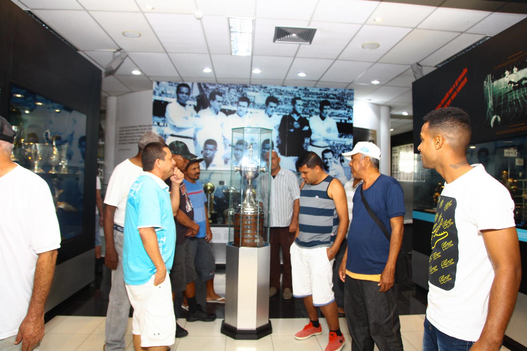 homens olham para troféus no memorial do Santos #pracegover