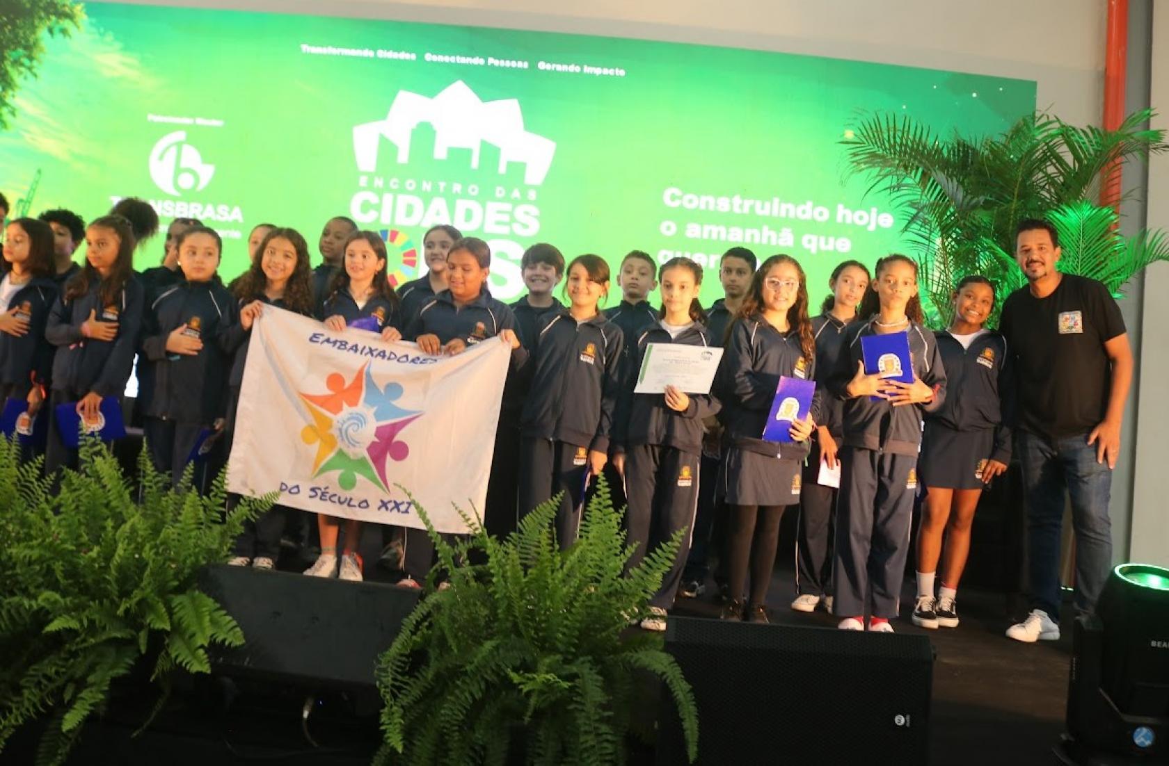crianças seguram bandeira em palco #paratodosverem