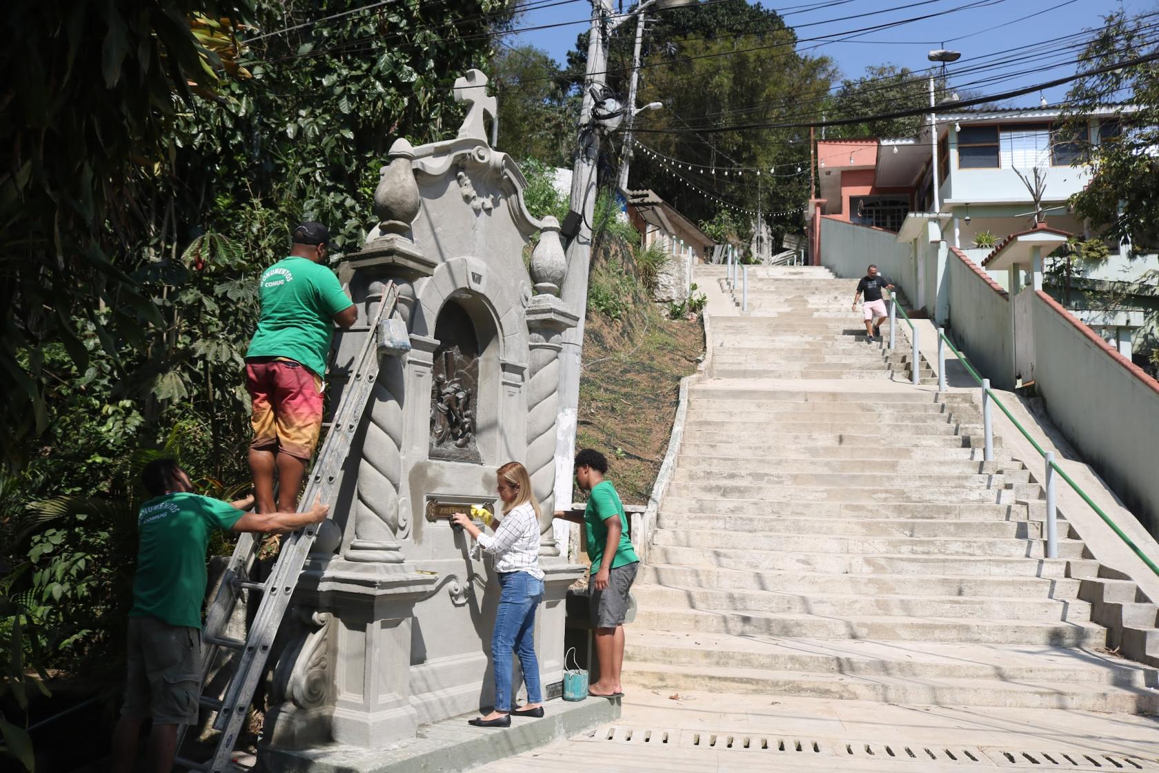 quatro pessoas em torno de um nicho junto à escadaria de morro. #paratodosverem