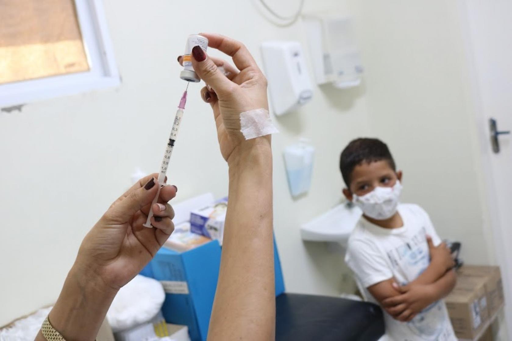 mulher prepara vacina enquanto menino observa #paratodosverem