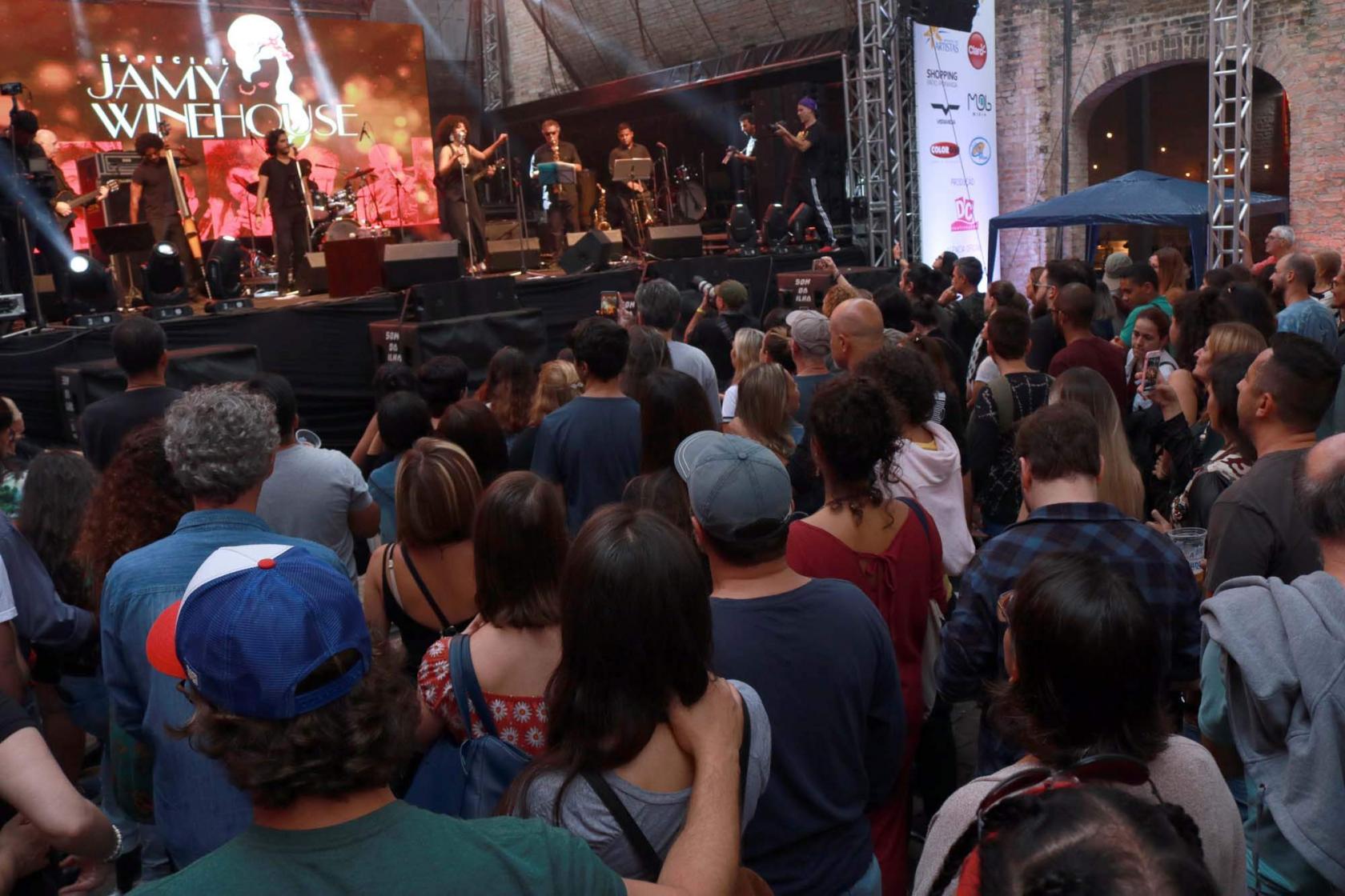 Show no Arcos do Valongo com público assistindo apresentação de conjunto no palco. #Pracegover