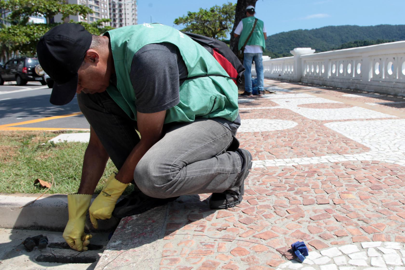 técnico da saúde coloca produto em ralo na orla #pracegover 