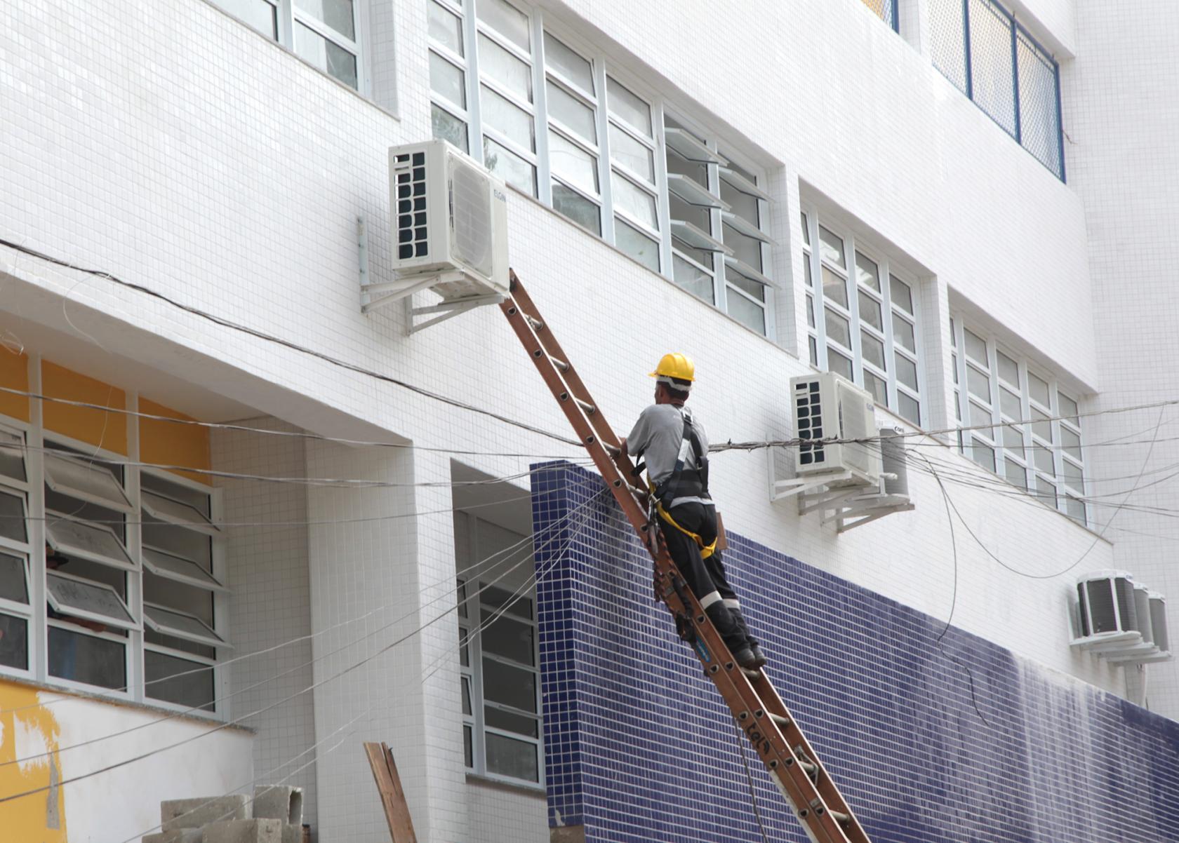 Homem em escada trabalha em parede de escola #pracegover 