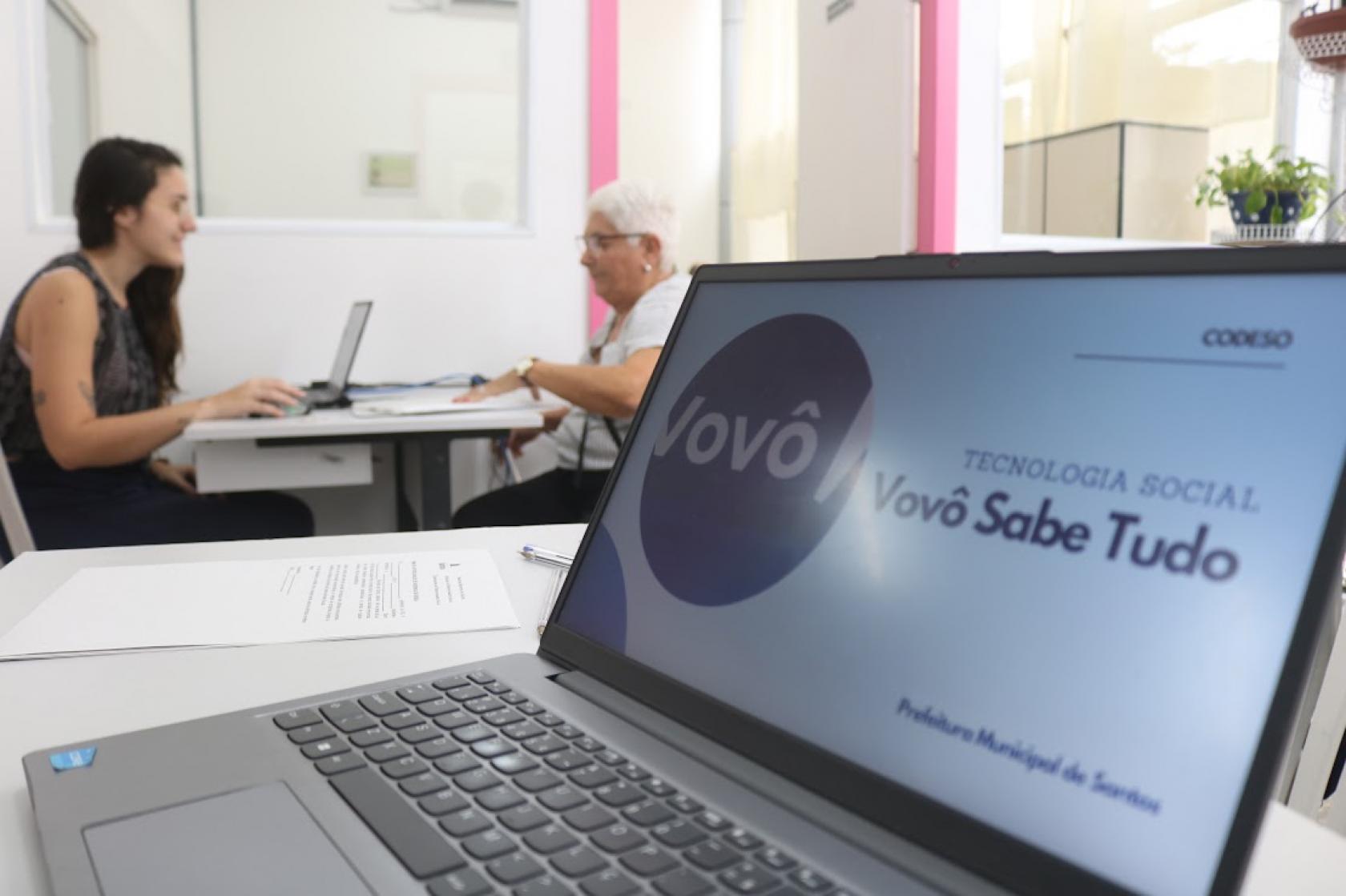 idosa faz inscrição com computador em primeiro plano #paratodosverem