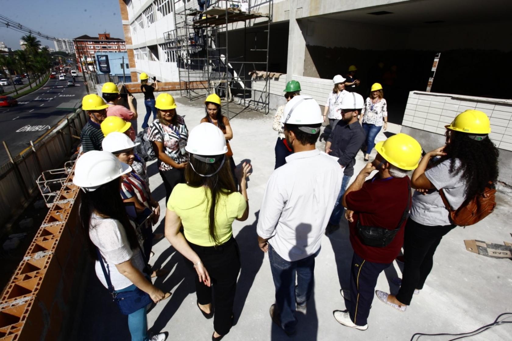 visitantes de capacete estão em círculo na obra #pracegover