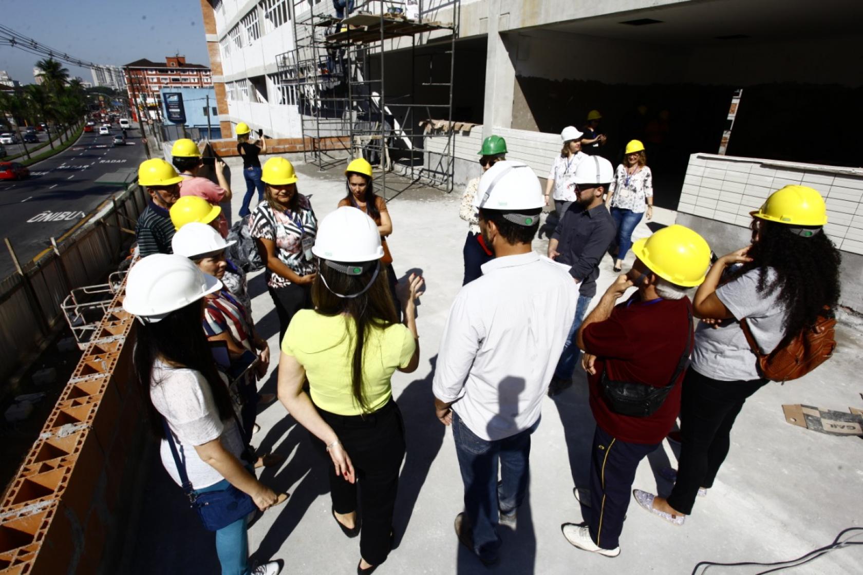 visitantes de capacete estão em círculo na obra #pracegover 