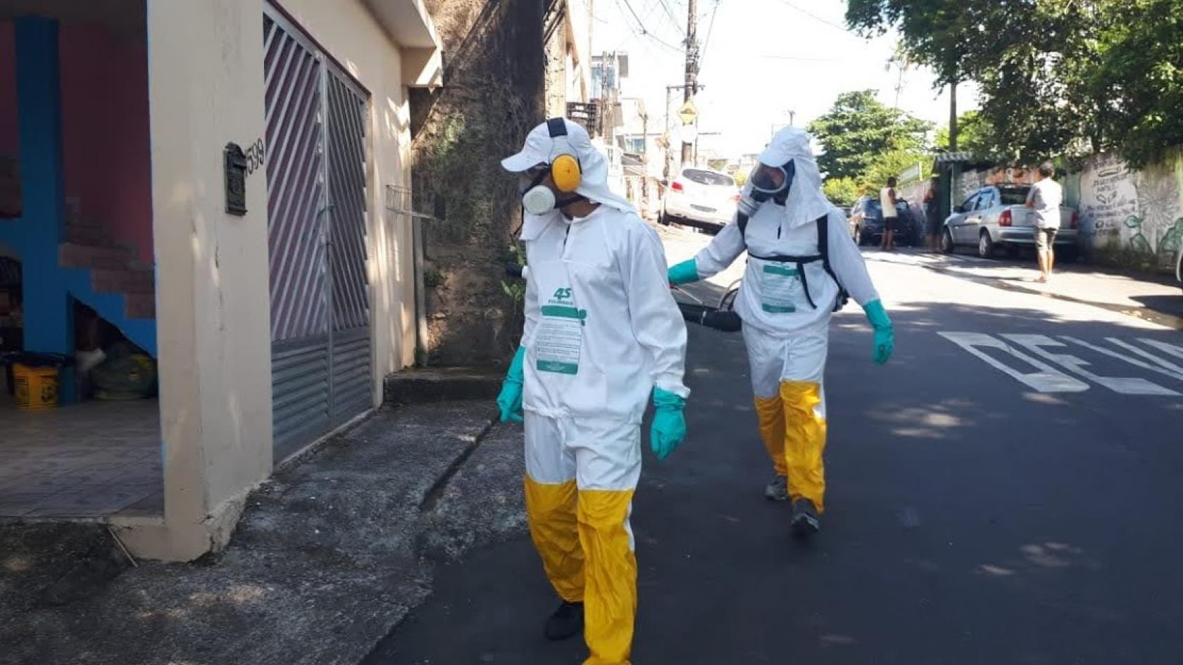 agentes com roupas de proteção nebulizam em rua #paratodosverem