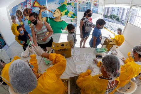 pessoas se aproximam de mesa onde técnicos fazem testes  #paratodosverem