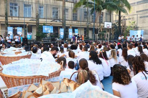 Voluntários sentados no pátio da escola à frente de palco montado no local