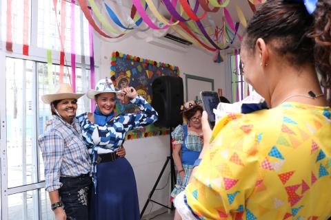 Duas mulheres com trajes de festa junina posam para foto tirada por outra mulher fantasiada