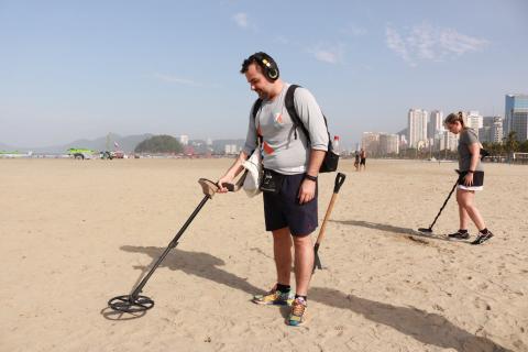 rapaz usa aparelho para detectar metal na areia #pracegover