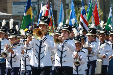 Banda escolar com integrantes fardados e soprando seus instrumentos. #Pracegover