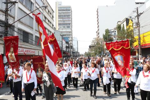 Procissão passa pela rua. Fieis seguram bandeiras. #Pracegover