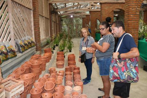 Um homem e duas mulheres observam vasos de orquídeas em área fechada do orquidário