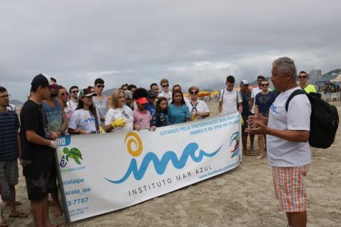 Pessoas agrupadas param sobre a areia segurando uma grande faixa onde se lê IMA - instituto mar azul