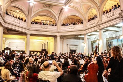 Público assiste apresentação de orquestra no salão e nas galerias do primeiro andar do Museu do Café. #Pracegover