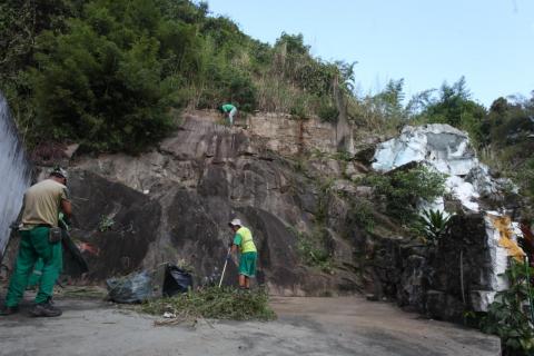 Homens limpam área próxima a gruta. #Pracegover