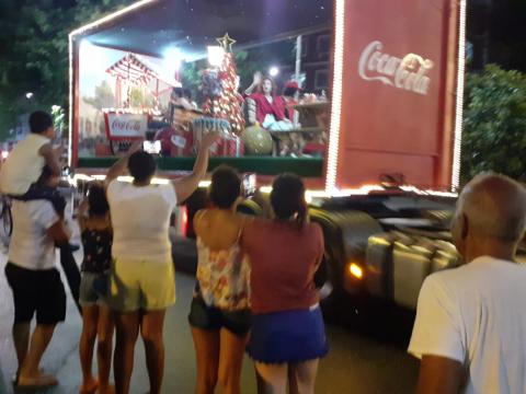 Público animado na rua ao observar veículo com cenário de Natal. #Pracegover