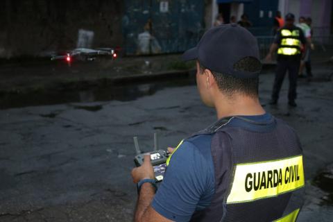 Guarda municipal maneja controle remoto de drone que está à sua frente. #Pracegover