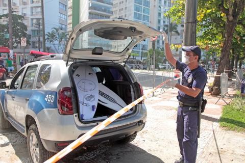 Guarda Municipal está com a mão na porta aberta de um bagageiro de carro onde há duas pranchas. O carro é da GCM. #Paratodosverem